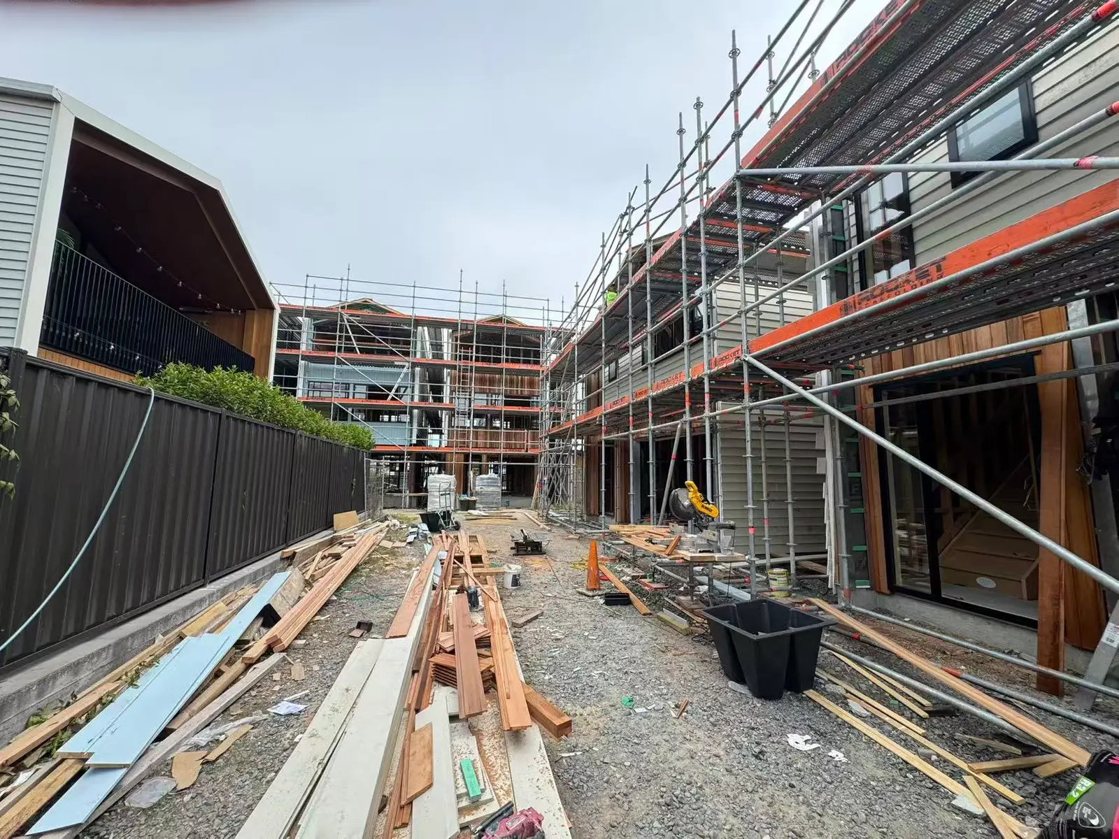 Site laneway between scaffolded townhouses with timber and cladding laid out