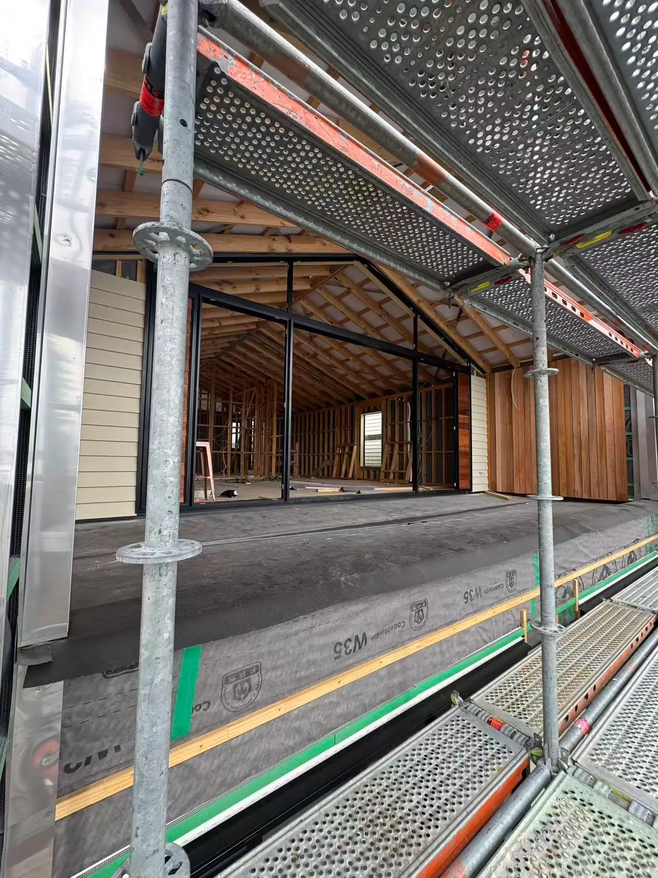 View from the scaffold deck into a framed upper level with a gable window installed