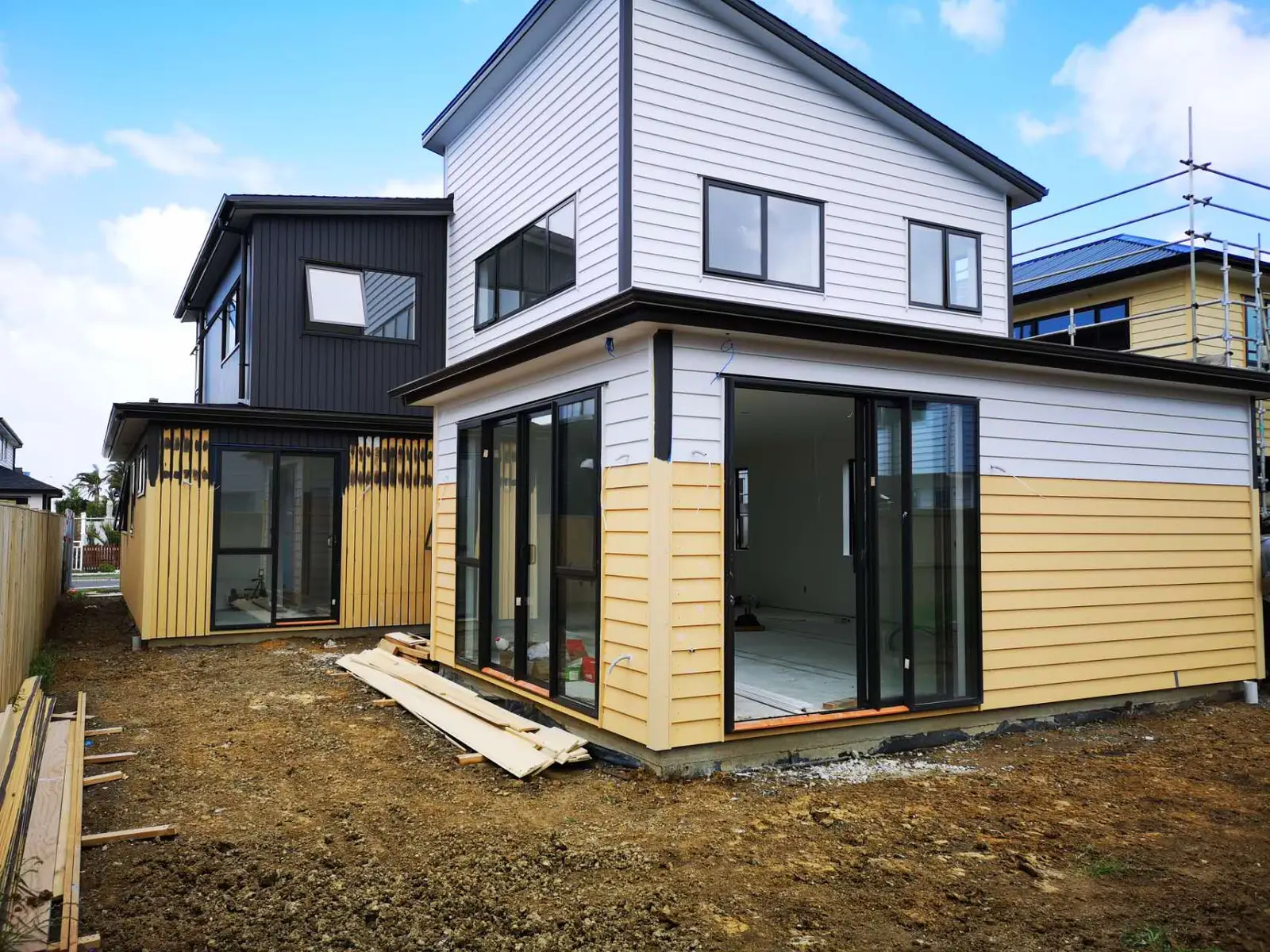 Rear of a two-storey home during cladding, with black-framed sliding doors fitted