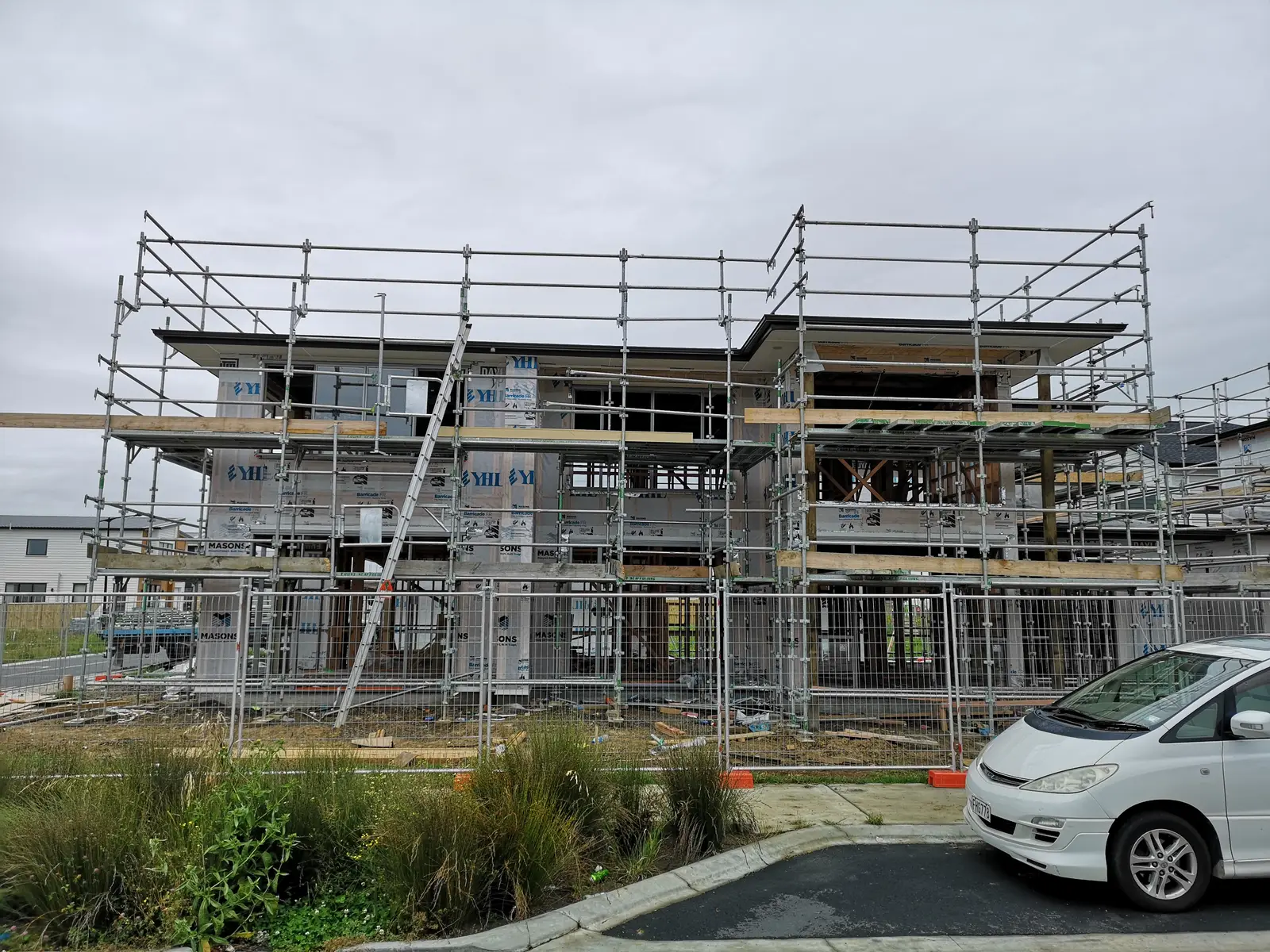 Two-storey home under construction behind scaffolding and building wrap