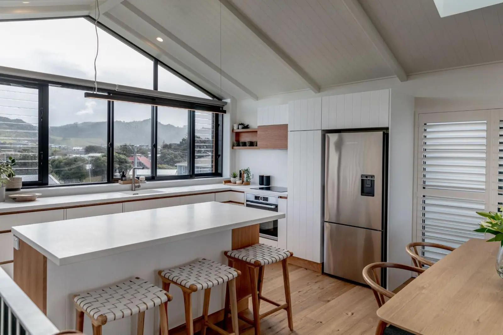 Townhouse kitchen with a white island under a raked ceiling and a gable window looking out to the hills
