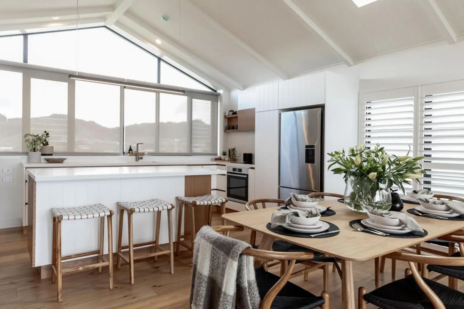 Open-plan kitchen and dining area with woven bar stools and a set timber table