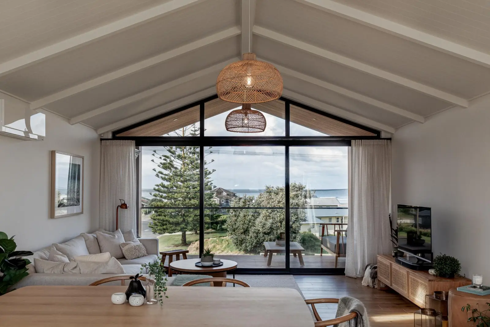 Living room with exposed ceiling rafters and a full-height gable window opening to a sea-view deck